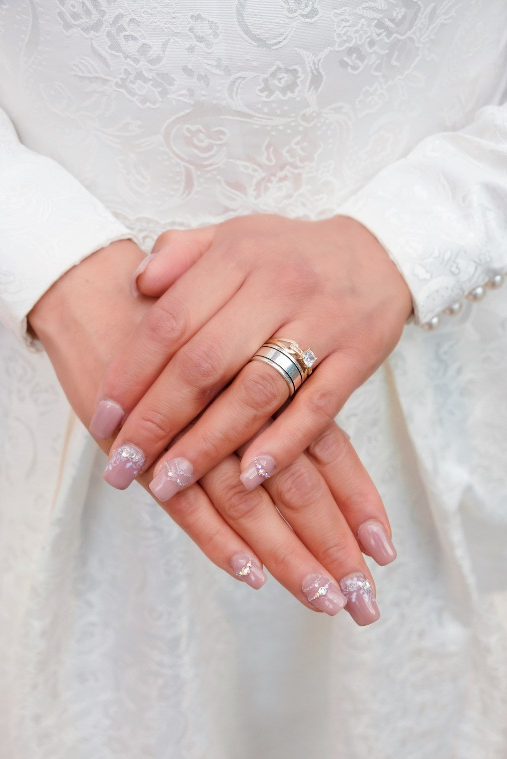 Close-up of a bride's hands showing off her classy wedding nails and rings against a lace dress backdrop.